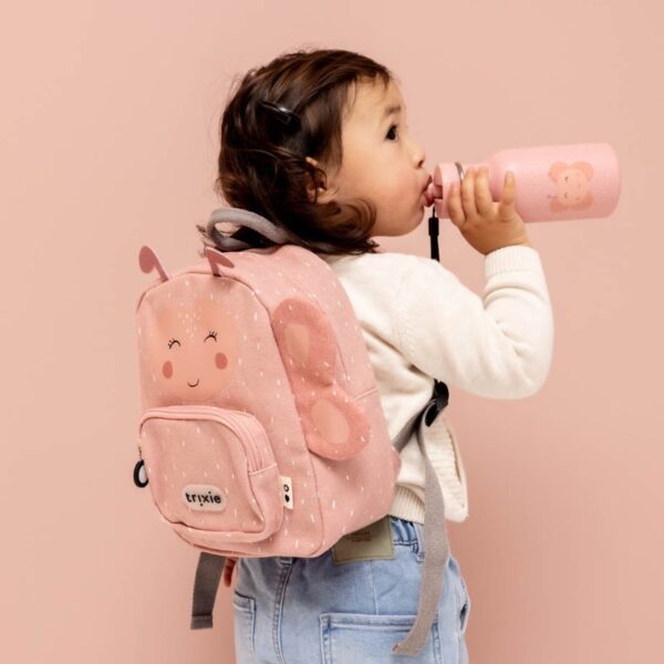 meisje met bruine haren, witte pull en jeans heeft het roze rugzakje van trixie in de vorm van een vlinder op haar rug en drinkt van een roze drinkfles met vlinder op van Trixie